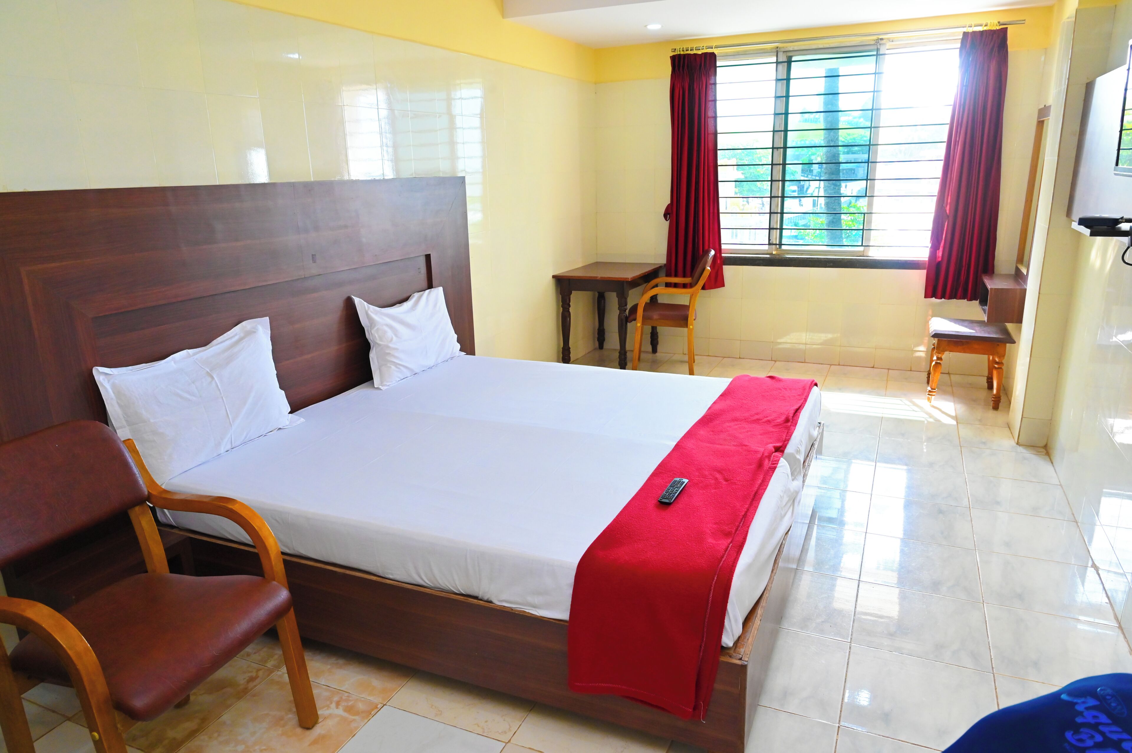 A hotel room with a large bed, wooden headboard, two bedside tables, a desk, a chair, and a window with curtains.