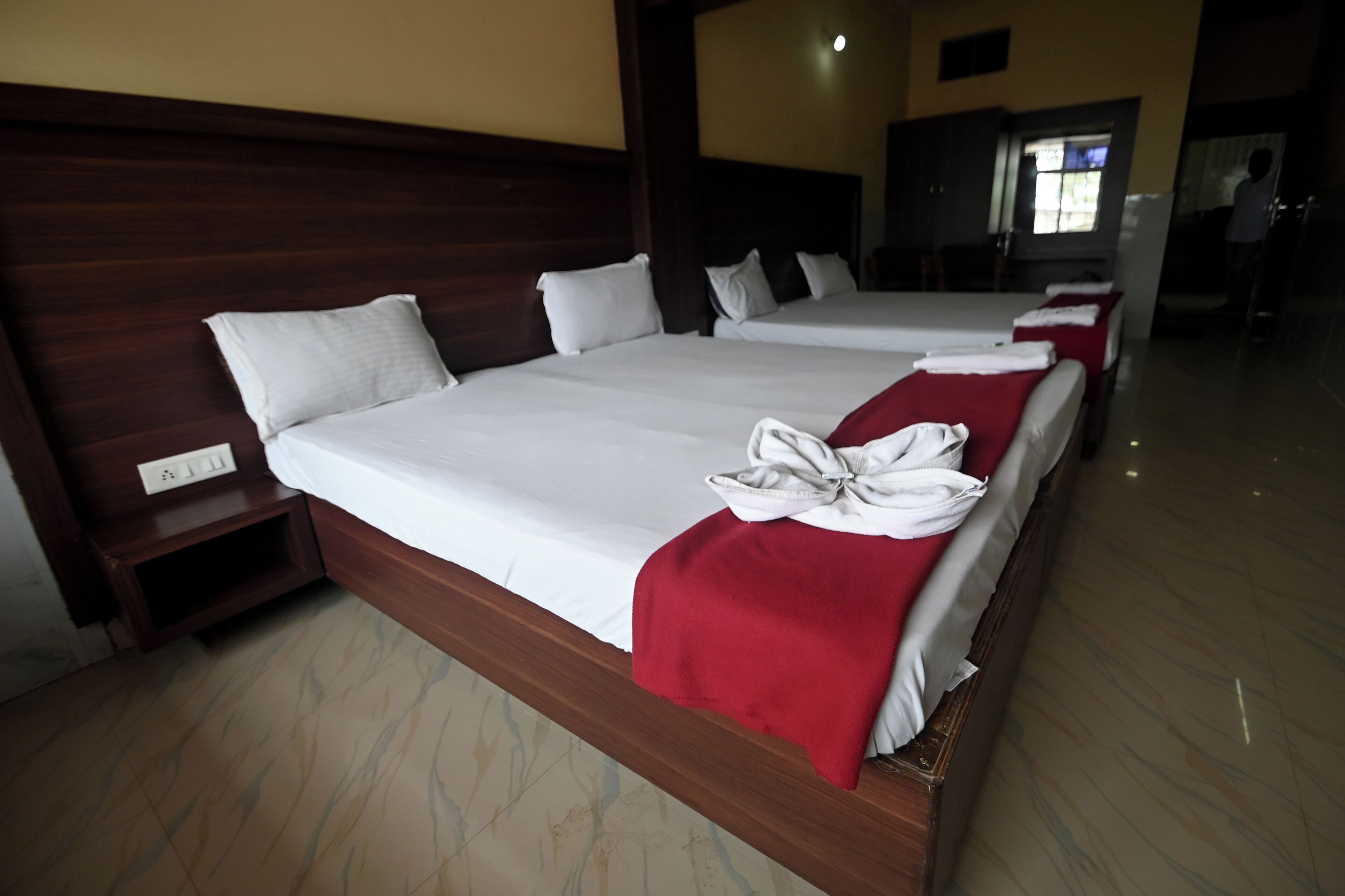 Ein Hotelzimmer mit zwei Betten, Holz-Kopfteilen, weißen Leinentüchern und einer roten Tagesdecke auf einem Bett.