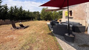 A backyard with outdoor furniture, a red umbrella, and a stone wall. - Une Belle Histoire holiday home (Sainte-Livrade-sur-Lot)