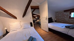 A bedroom with two beds, a wooden ceiling, a brick wall, and a window. - Une Belle Histoire holiday home (Sainte-Livrade-sur-Lot)