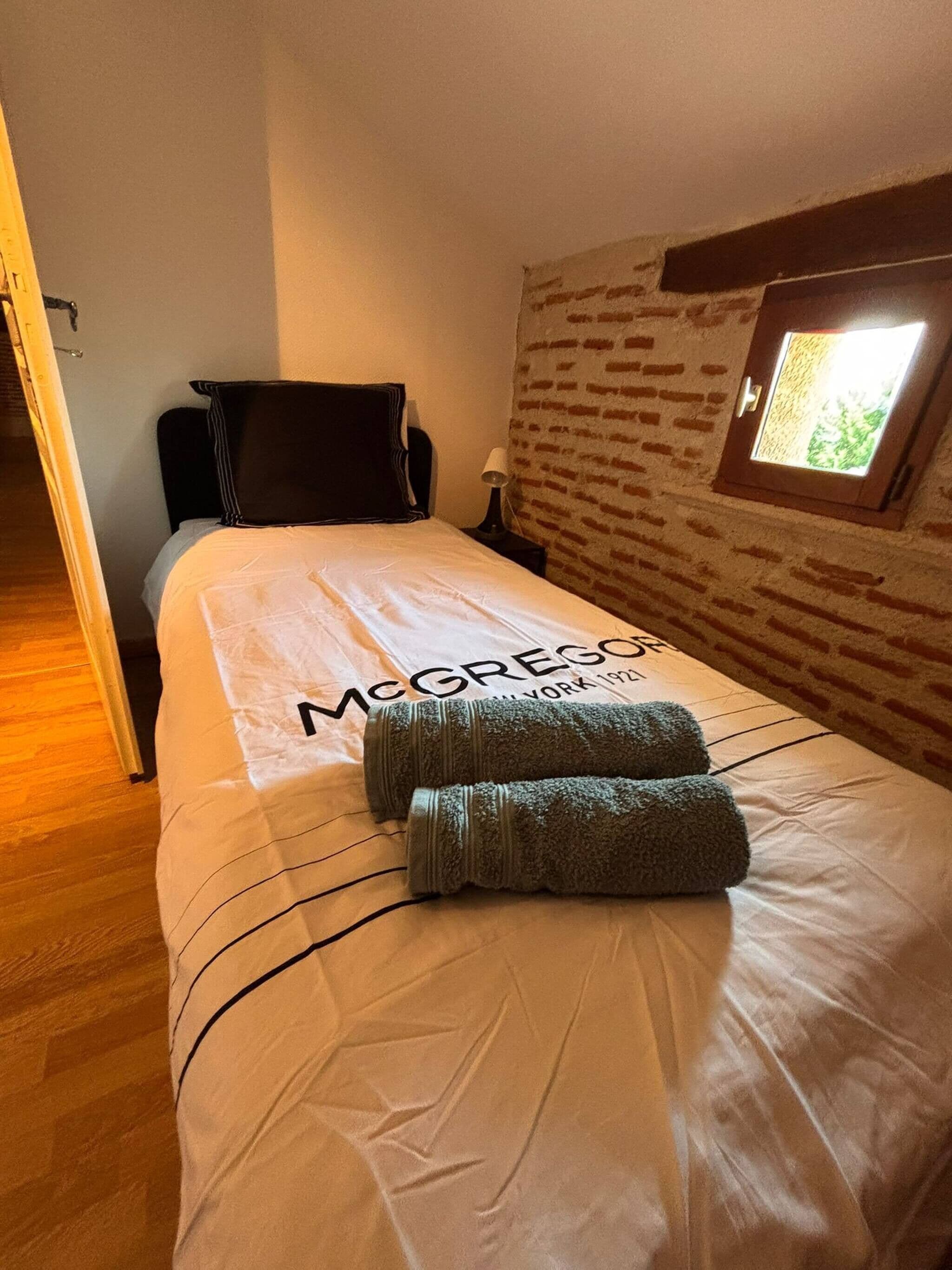 Quarto de hotel com cama, mesa de cabeceira, abajur, janela com vista e porta.