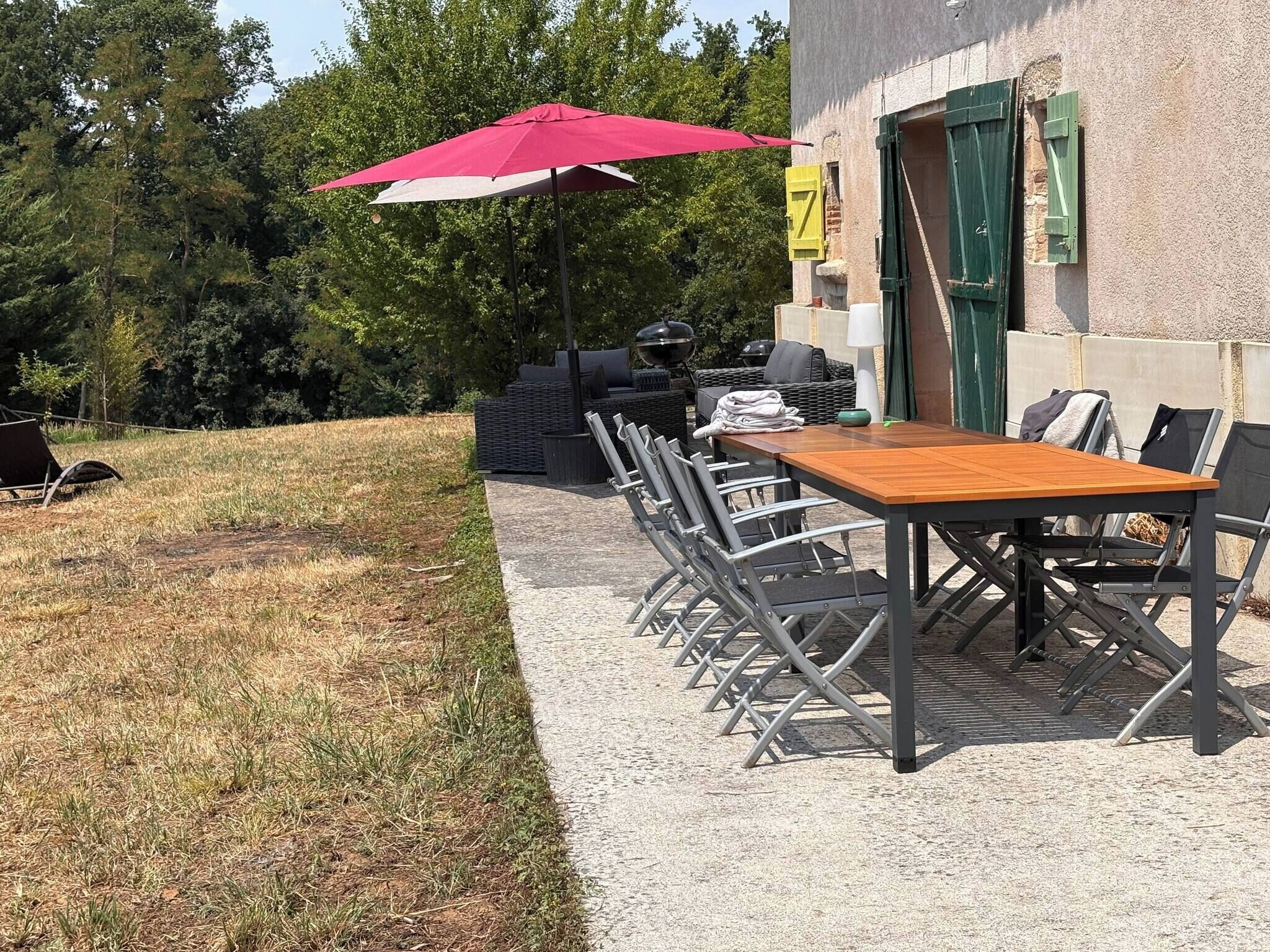 An outdoor dining area with a table and chairs, a red umbrella, and a grill.