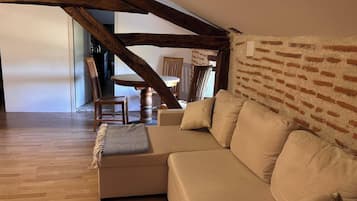 En hyggelig stue med en beige sofa, træbjælker og en murstensvæg.