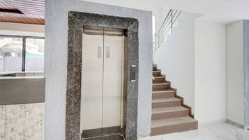 Un ascensor moderno con pantalla digital, suelo de mármol y escalera con barandilla de metal.