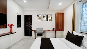 Quarto de hotel moderno com uma cama, uma escrivaninha, uma cadeira, uma televisão e obras de arte na parede.