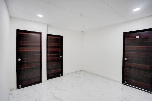 A hallway with three dark wooden doors, white walls, and a marble floor. - Super Collection O Omkar Nagar Nagpur (Nagpur)