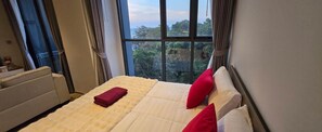 A bedroom with a bed, a window with curtains, and a view of greenery outside. - Sea View Room Great Location Beach Front (Muang Pattaya)