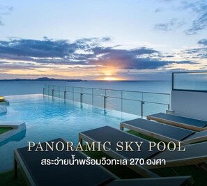 Ein Panoramapool im Himmel mit Sonnenuntergangsblick, Liegestühlen und einer Glasbrüstung.
