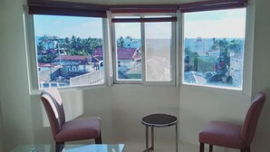 Een hoekappartement met twee stoelen, een klein tafeltje en uitzicht op een woonwijk door grote ramen.