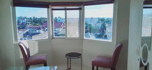 Ein Eckzimmer mit zwei Sesseln, einem kleinen Tisch und Blick auf eine Wohngegend durch große Fenster.