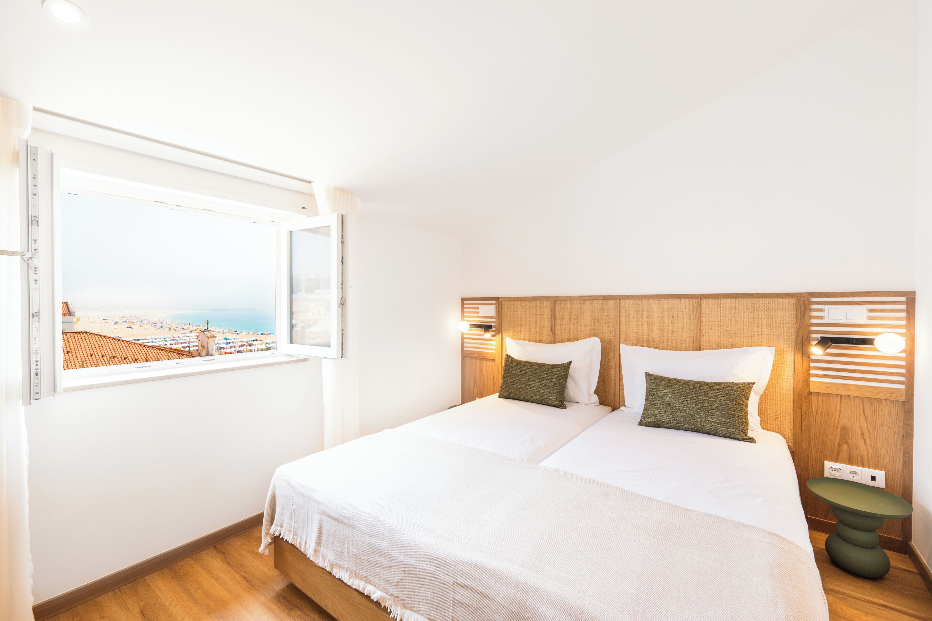 Habitación de hotel con una cama grande, vista a la playa y cabecera de madera.