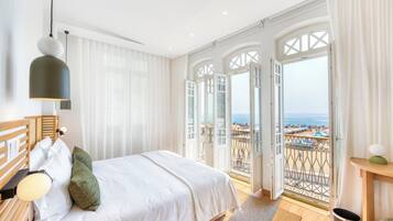 Habitación de hotel con cama, mesita de noche, lámpara, vista a la playa y balcón con barandilla.