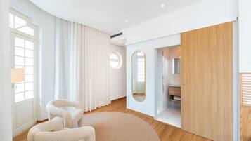 Een moderne hotelkamer met een groot raam, een ronde spiegel, een houten deur en een zithoek met een rond tapijt.