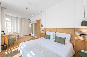 Habitación de hotel moderna con una cama grande, un área de descanso con una silla y una mesa, y vistas al exterior.