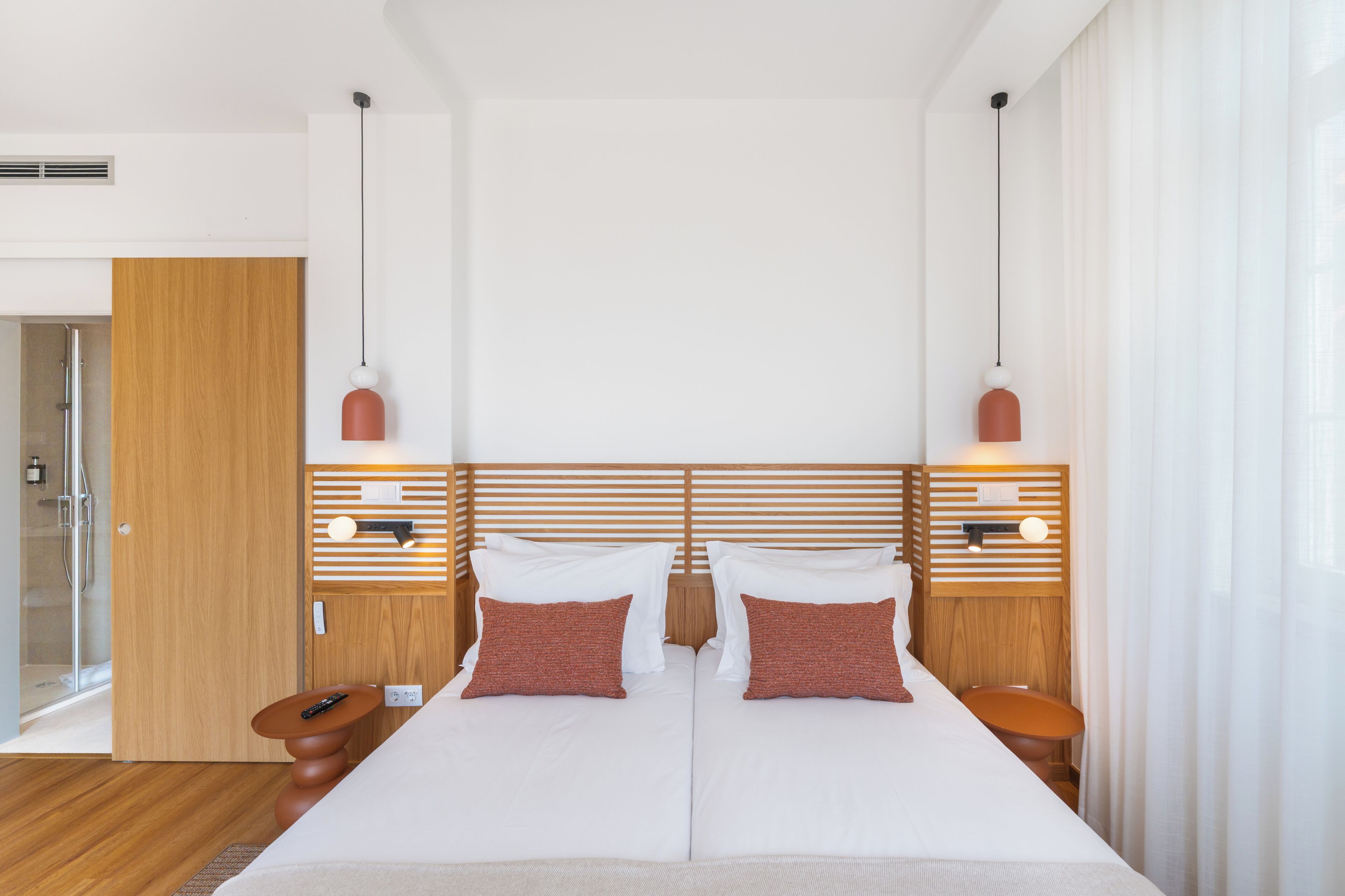 Una habitación de hotel moderna con una cama grande, dos mesitas de noche, un cabecero de madera y lámparas colgantes.