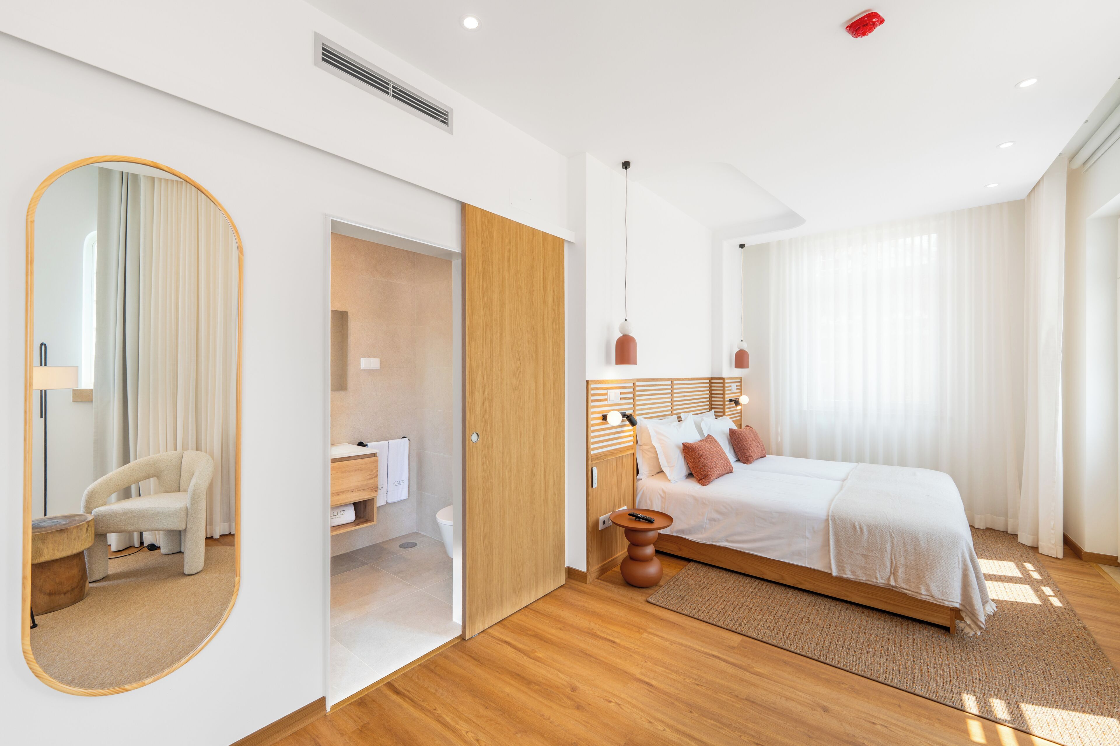 Quarto de hotel moderno com cama, espelho, banheiro e piso de madeira.
