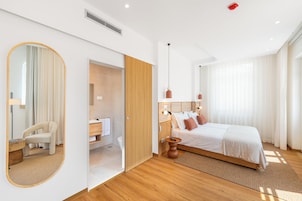 Una habitación de hotel moderna con cama, espejo, baño y piso de madera.