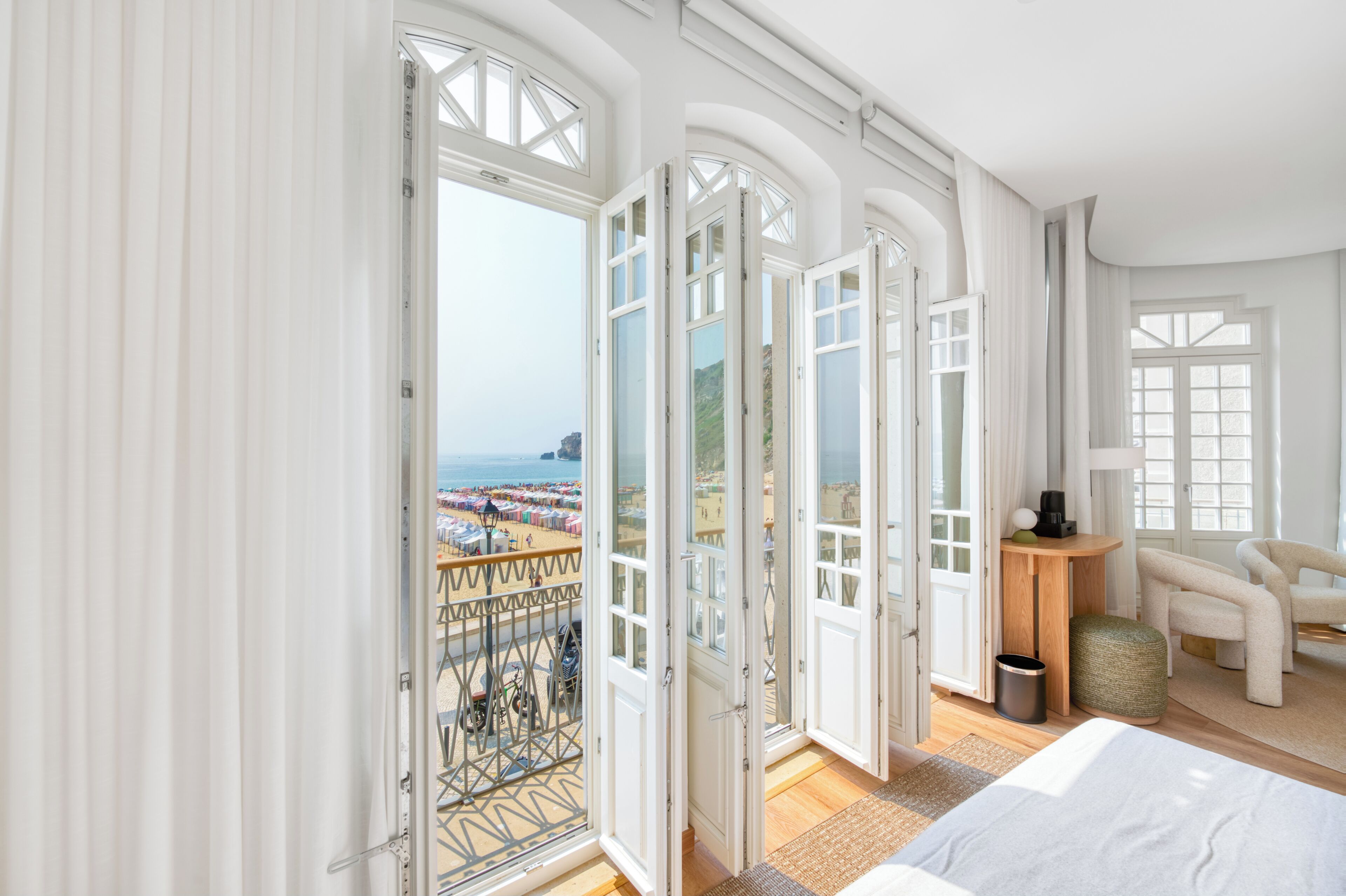 A hotel room with a large balcony, a bed, a chair, and a view of the beach.