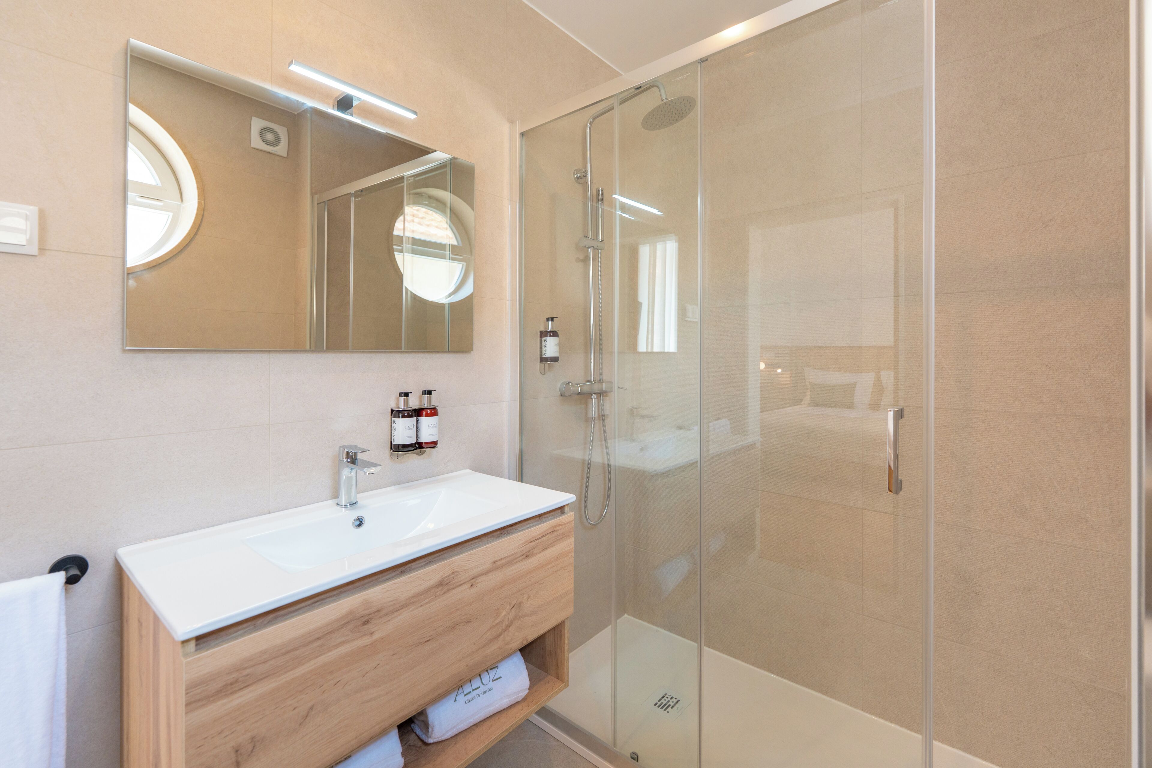 A modern bathroom with a glass shower enclosure, a white sink, and a wooden vanity.