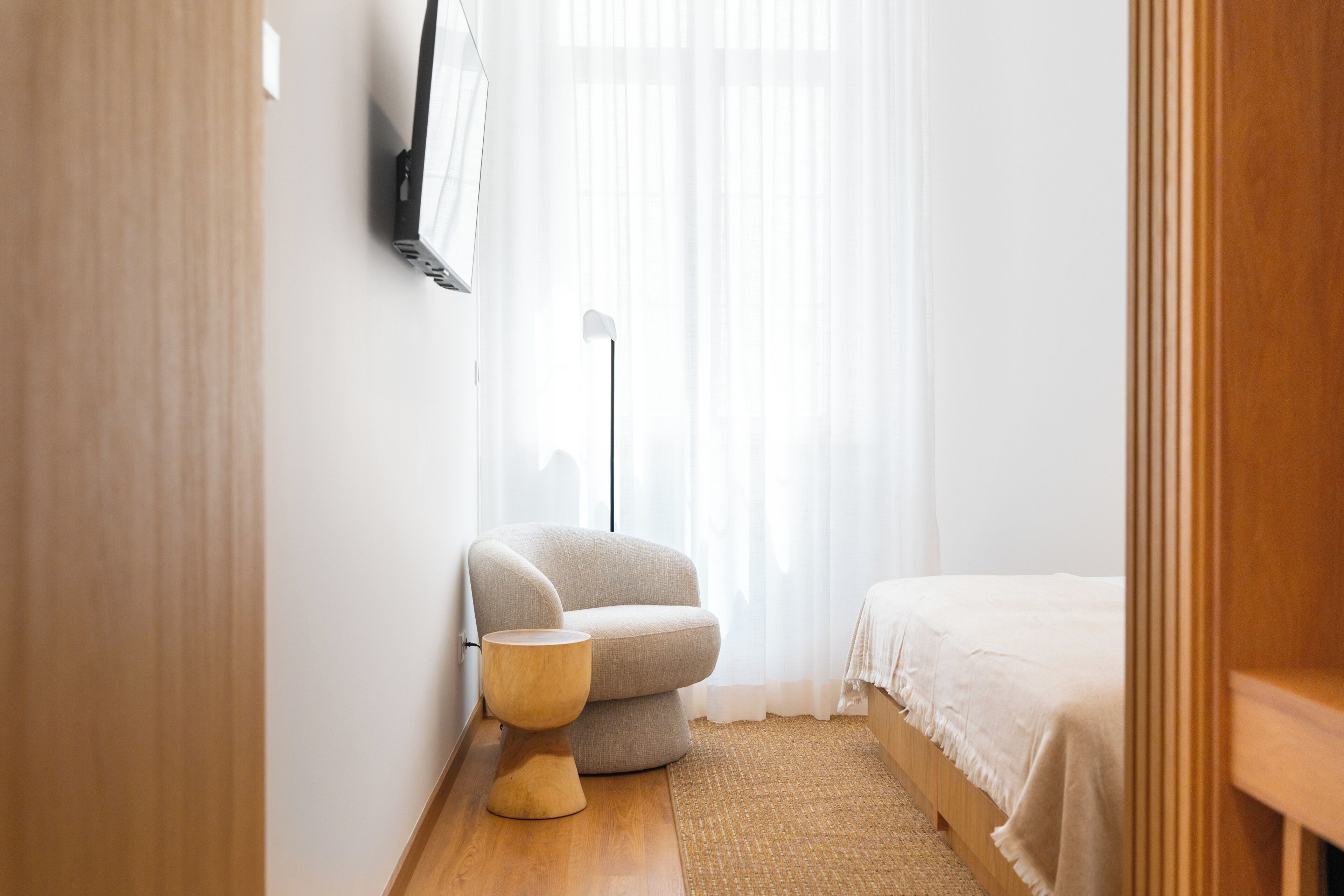 Un dormitorio con una cama, una silla, una lámpara de pie y una mesita.