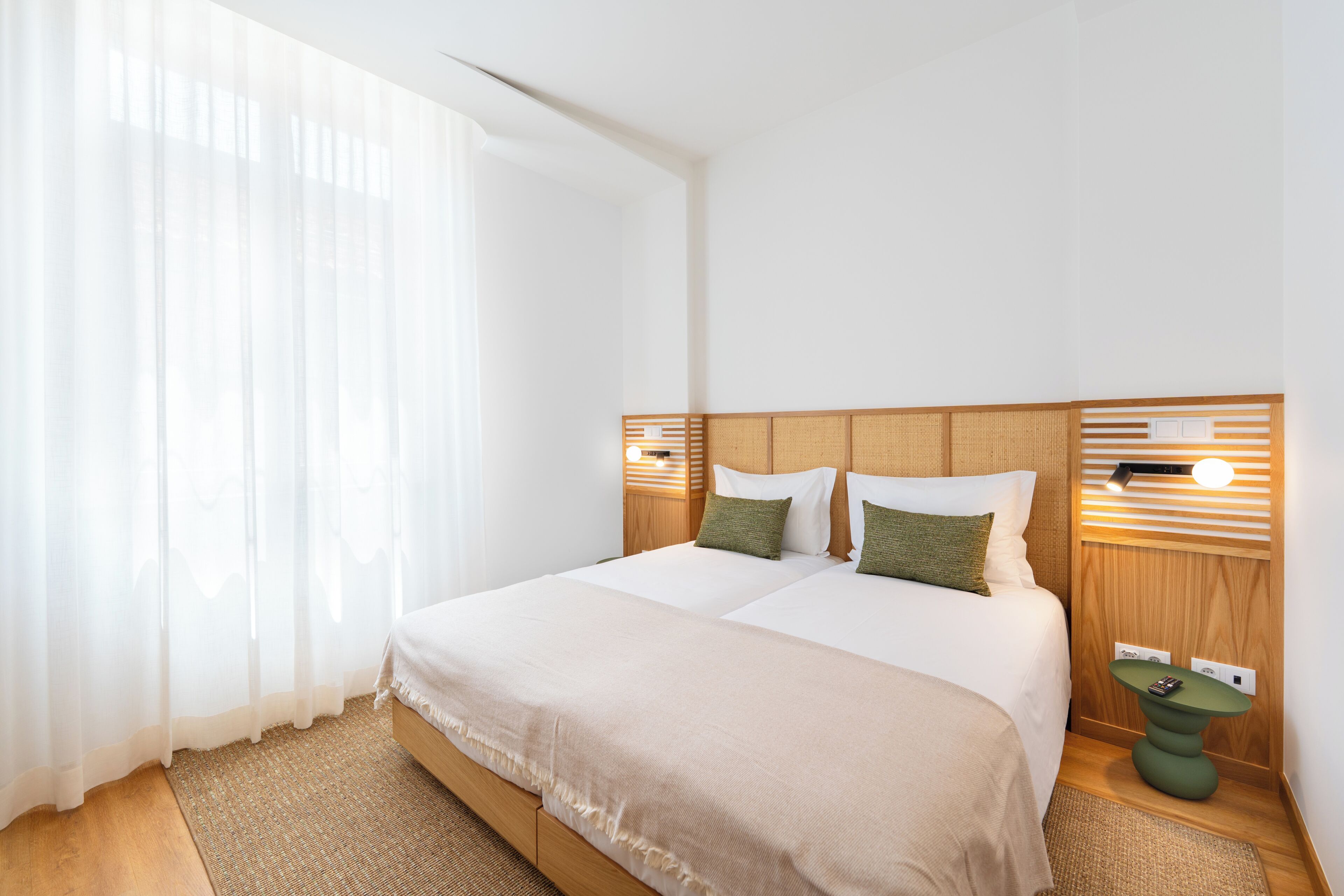 A hotel room with a large bed, two pillows, a bedside table, and a wall-mounted light fixture.