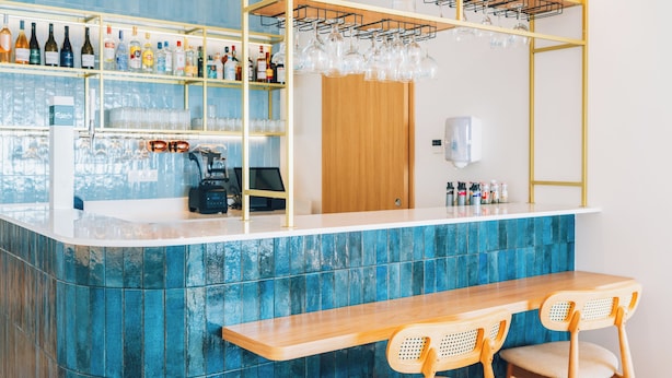 Zona de bar con mostrador, estantes con botellas y un área de asientos con sillas.