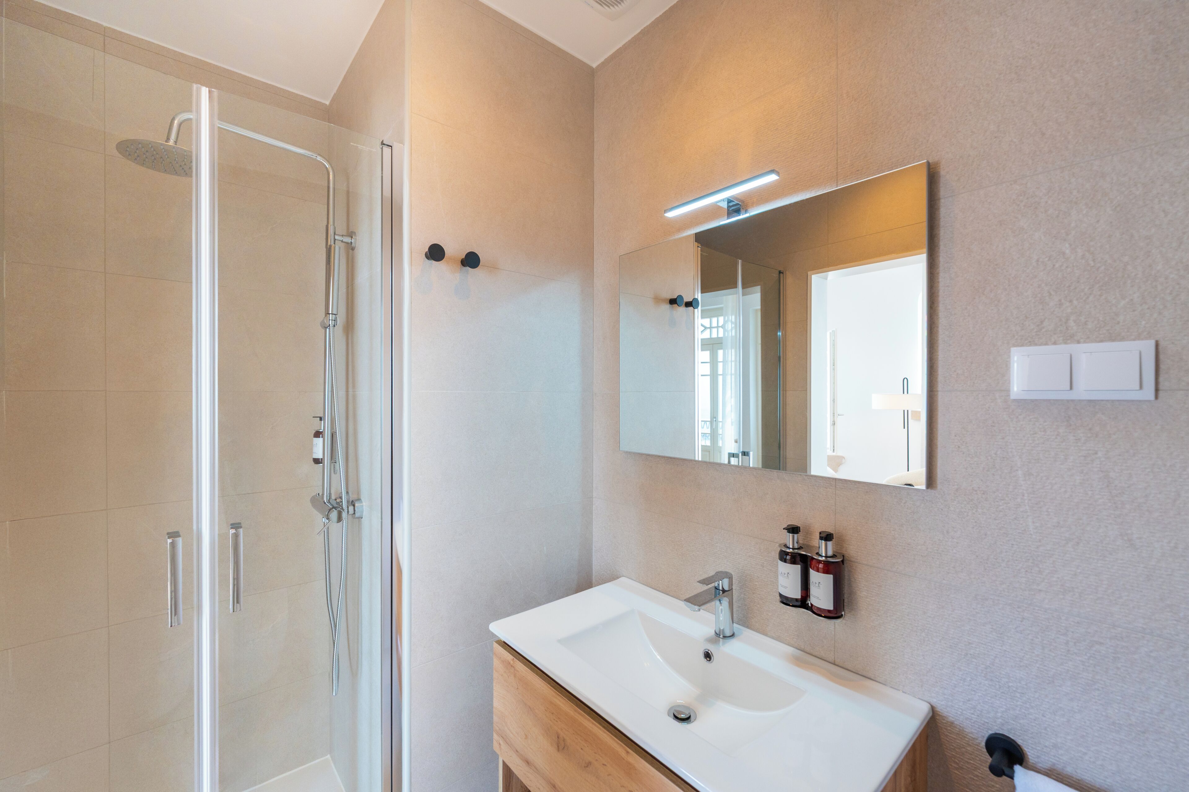 Un bany modern amb una dutxa de vidre, un lavabo blanc i un mirall sobre la petita taula.
