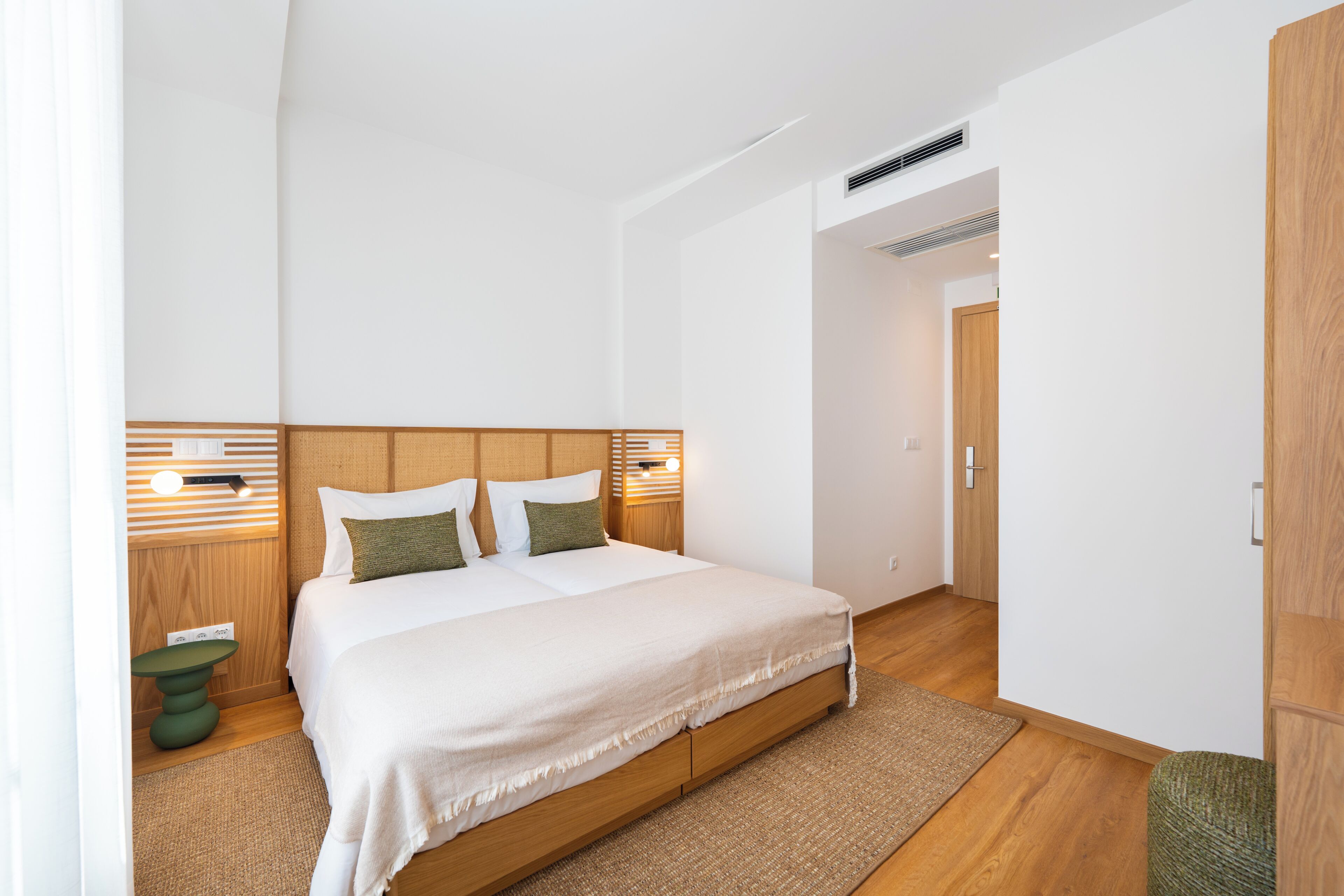 A modern bedroom with a large bed, wooden headboard, and a bedside table with a lamp.