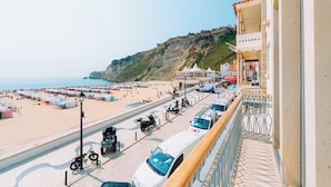 Vista desde la playa con un paseo pavimentado, vehículos estacionados y sombrillas de playa.