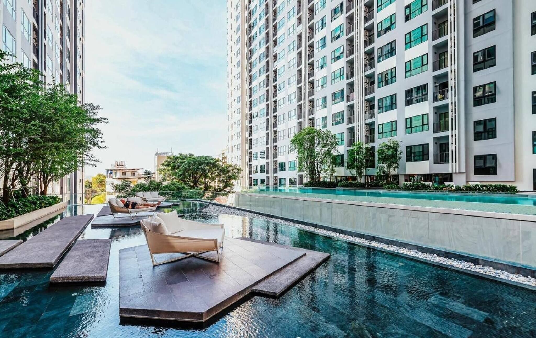 A rooftop infinity pool with lounge chairs, surrounded by high-rise buildings and greenery.