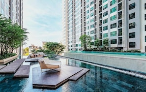 Une piscine à débordement située sur le toit, avec des chaises longues, entourée de gratte-ciel et de verdure.
