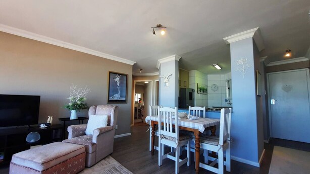 A living room with a television, a sofa, a dining table with chairs, and a kitchen area with cabinets and a refrigerator. - Amazing View For Less Bloubergstrand Beachfront (Cape Town)
