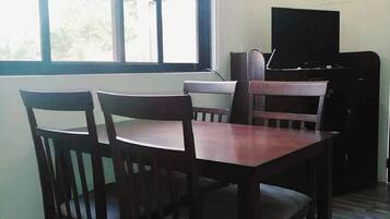 Huone, jossa on ruokapöytä ja -tuolit, televisio ja ikkuna, josta on näkymä vehreään maisemaan.