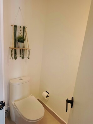 Et lille badeværelse med toilet, en hængende plantekurv i makramé og toiletpapirholder.