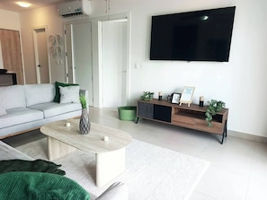 A modern living room with a sofa, coffee table, and a TV mounted on the wall. - Spacious 1-Bedroom Apartment with Shared Pool in Punta Cana (Punta Cana)
