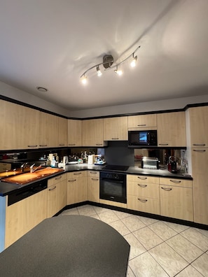 A modern kitchen with wooden cabinets, a black countertop, a built-in oven, and a microwave. - Villa la Hutte, Grand Piquey, Lège, Cap Ferret (Lège-Cap-Ferret)