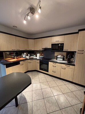 A modern kitchen with a central island, black countertops, and light wood cabinets. - Villa la Hutte, Grand Piquey, Lège, Cap Ferret (Lège-Cap-Ferret)