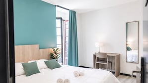 A hotel room with a bed, a desk, a chair, a mirror, and a window with curtains.