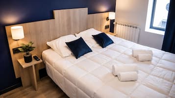 A hotel room with a large bed, two bedside lamps, a small table with a plant and remote, and a window with curtains.