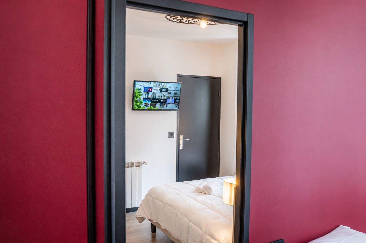 Een slaapkamer met een bed, een aan de muur bevestigde televisie en een deur naar een andere kamer.