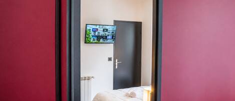 Une chambre à coucher avec un lit, un téléviseur fixé au mur et une porte donnant sur une autre pièce.