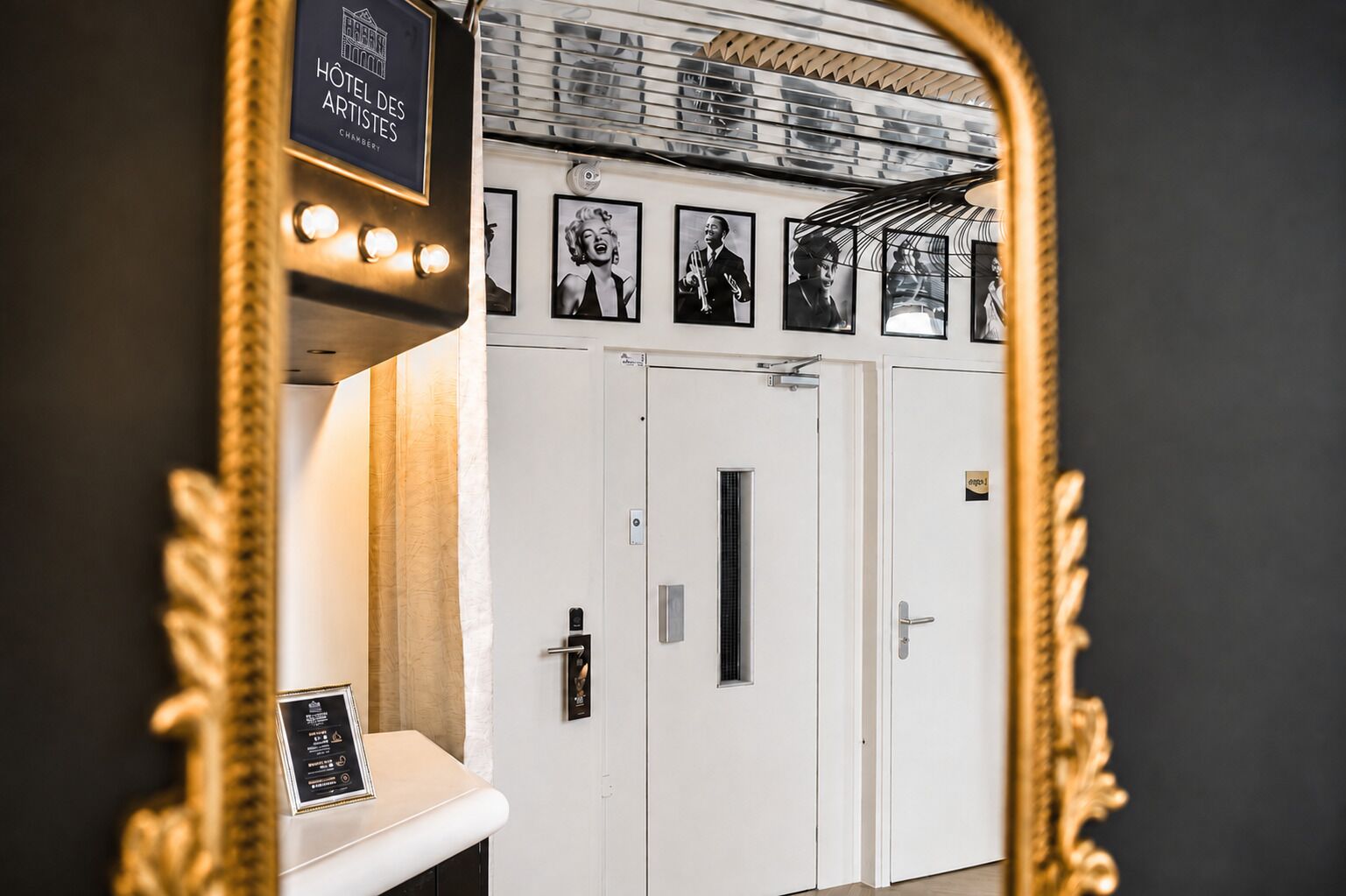A hotel room with a mirror reflecting a door, a framed picture, and a sign above the door.