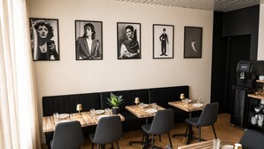 Un restaurante con asientos tapizados en negro, mesas de madera y sillas negras. Se observan cuadros enmarcados en la pared y una máquina de café en una esquina.