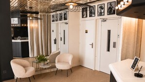 Habitación de hotel con kitchenette, una zona de estar con dos sillas, una mesita con una planta y un mostrador de recepción.