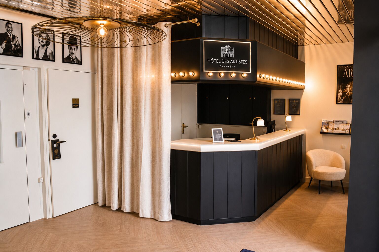 A hotel reception area with a counter, a sign reading 'Hôtel des Artistes Chambéry,' and a reception desk.