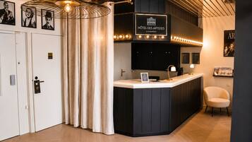 A hotel reception area with a counter, a sign reading 'Hôtel des Artistes Chambéry,' and a reception desk.