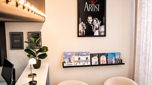 Habitación de hotel con escritorio, planta en maceta, cartel de 'The Artist' y estante con libros.