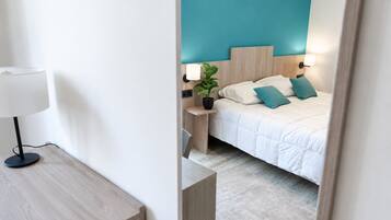 Una habitación de hotel con cama, mesita de noche, lámpara y una planta en maceta.
