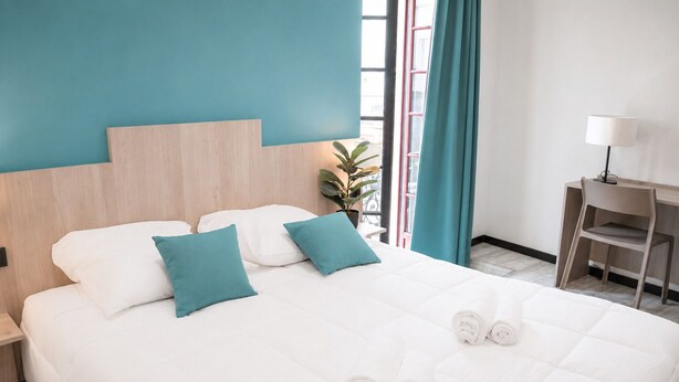 Habitación de hotel con cama, dos almohadas, escritorio, silla, lámpara y planta en maceta.