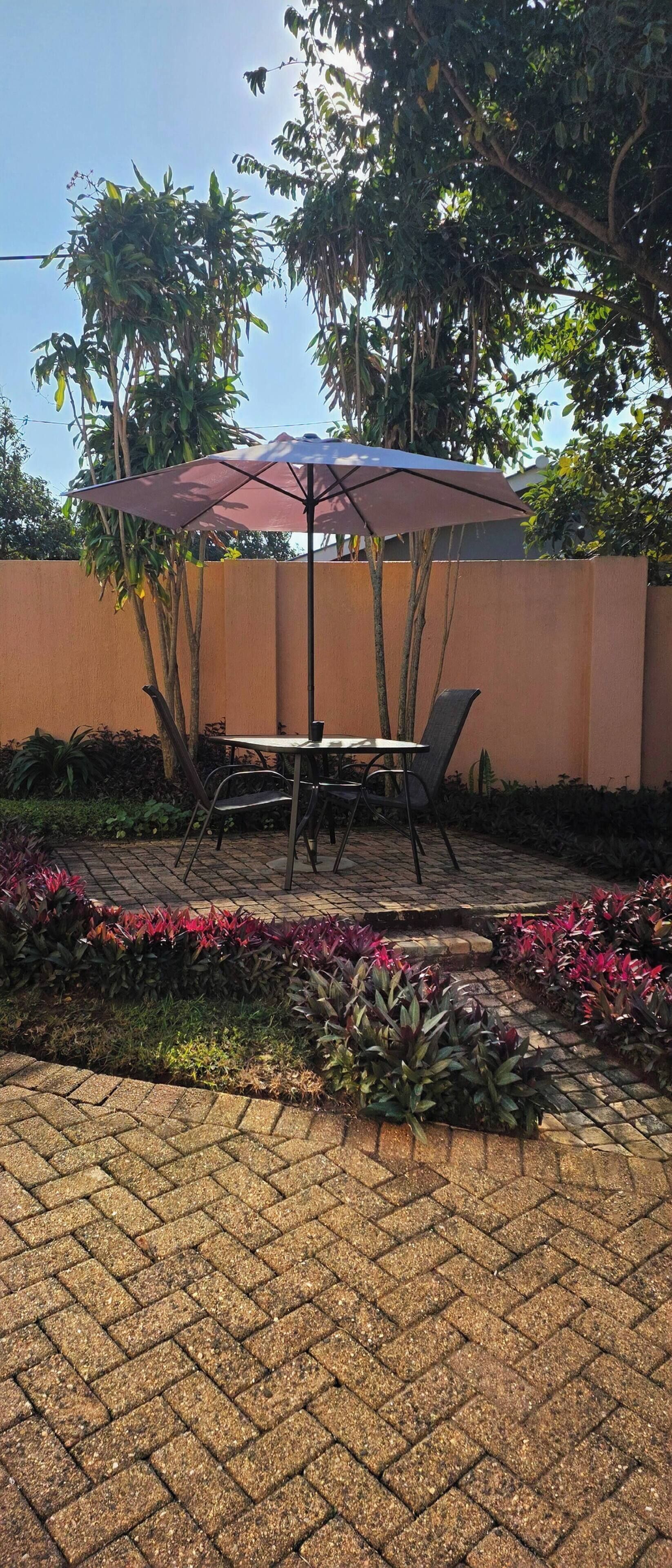 Un patio esterno con tavolo e sedie, un ombrellone grande e un vialetto in mattoni.